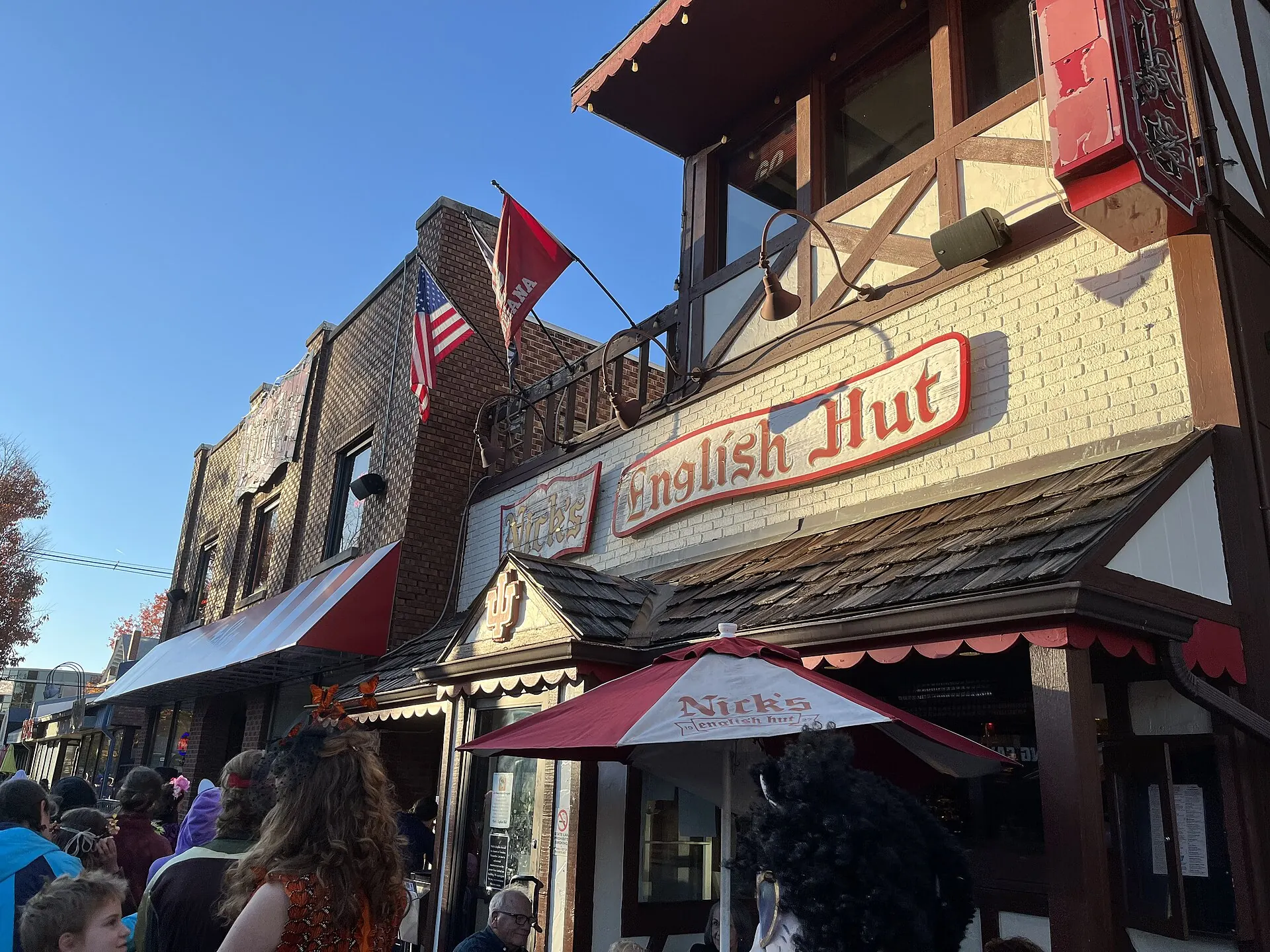 Nick’s English Hut, a Tudor-style storefront with a red script sign, a striped awning and a crowd out front
